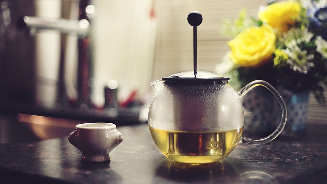 A tea pot is sitting on a counter next to a cup of tea.