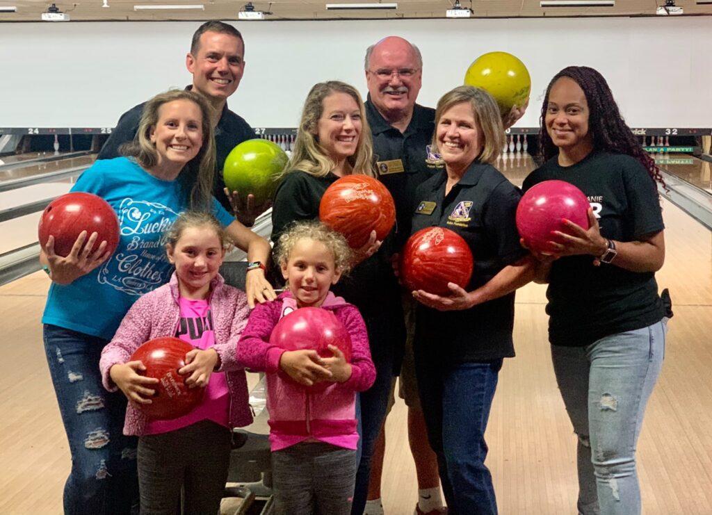 A group of people holding bowling balls in front of a wall.