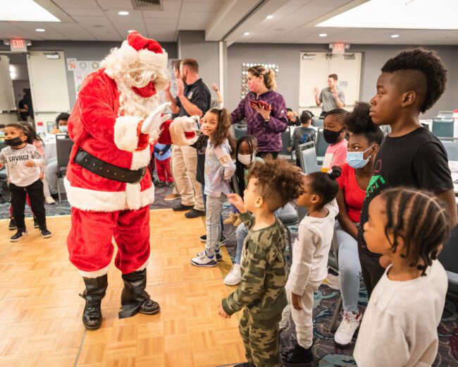 Santa Claus is standing in front of a group of children, spreading joy during the holiday season.