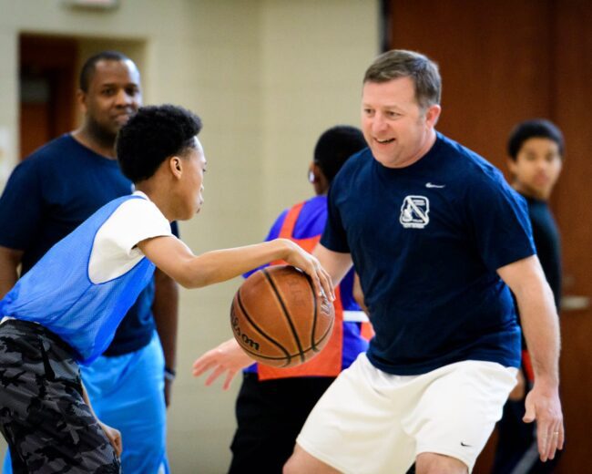 A man takes initiatives in teaching a group of boys how to play basketball.