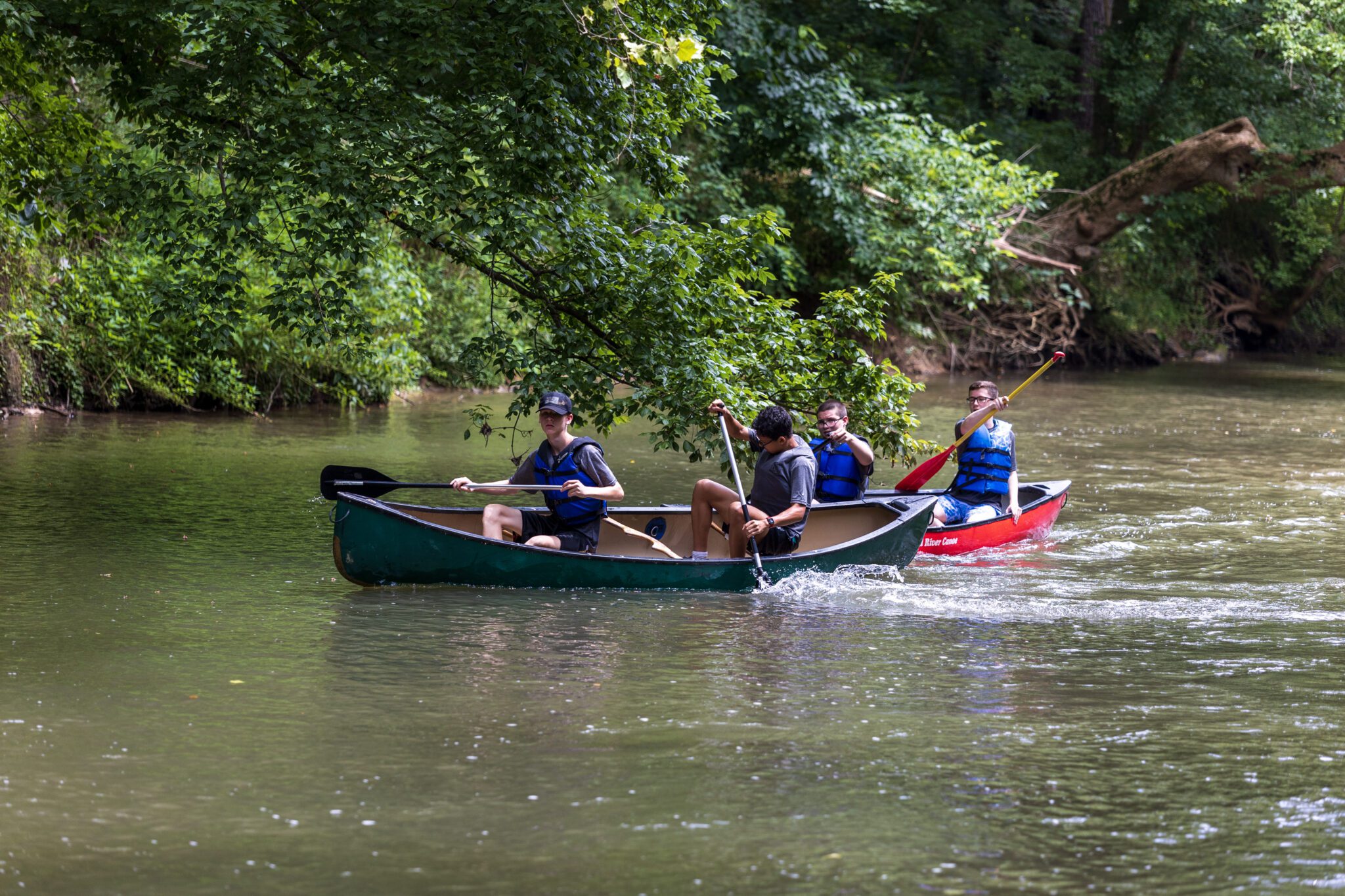 A group of people participating in the P.L.E.D.G.E. Leadership Program, navigating a river in a canoe.