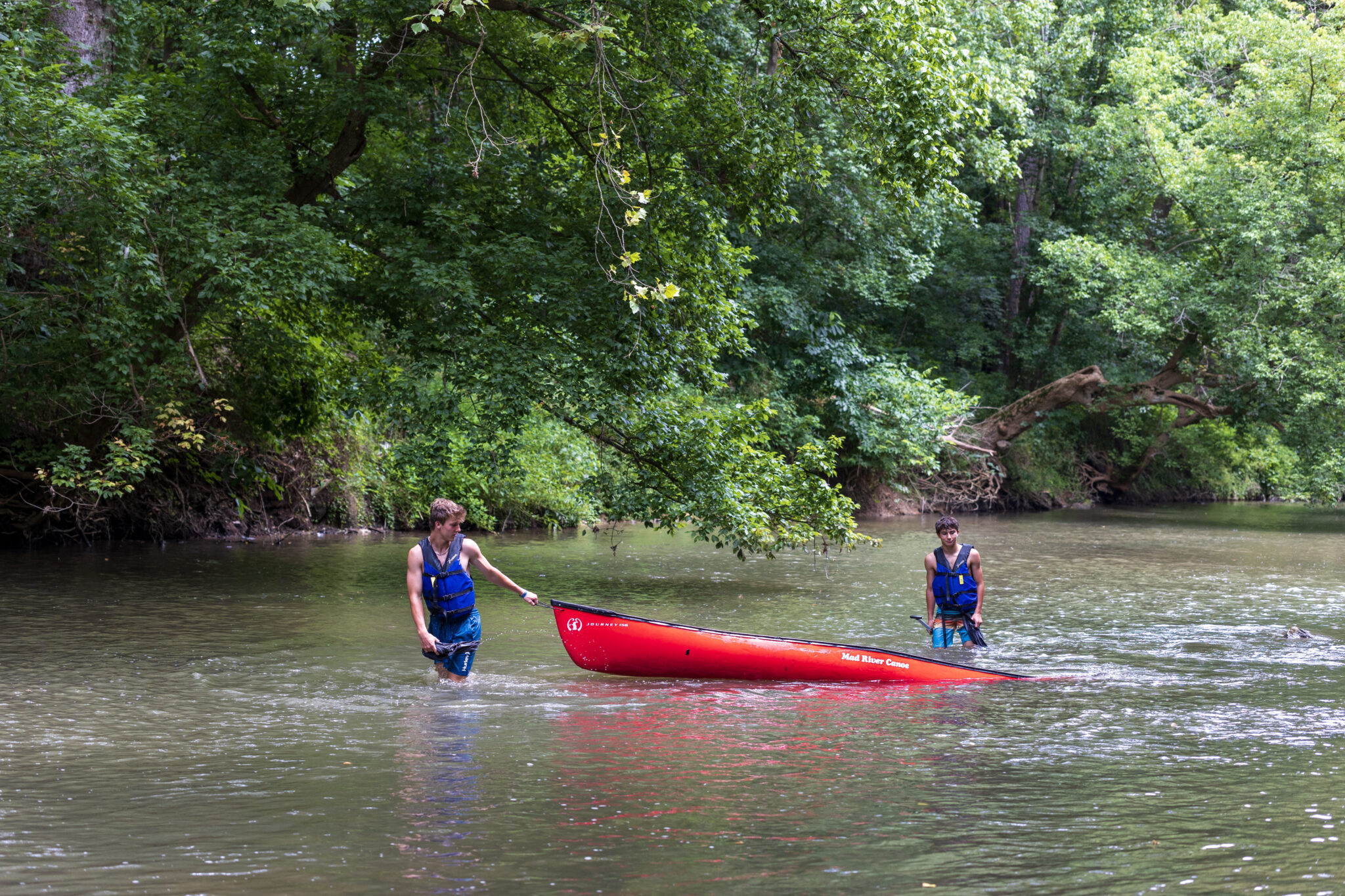 Two people participating in the P.L.E.D.G.E. Leadership Program, standing in a river with a red canoe.