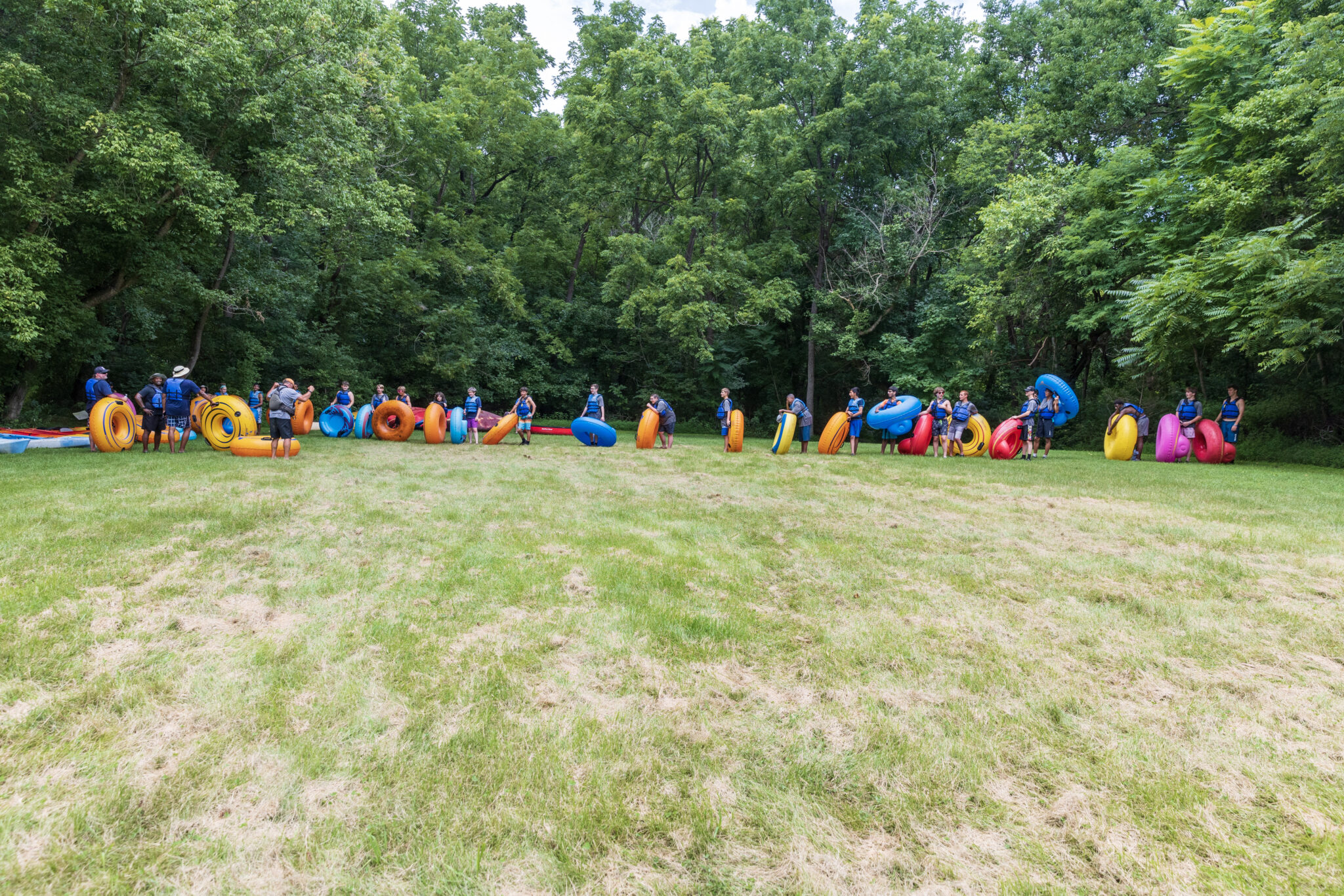 A group of people participating in the P.L.E.D.G.E. Leadership Program, standing in a grassy area with rafts.