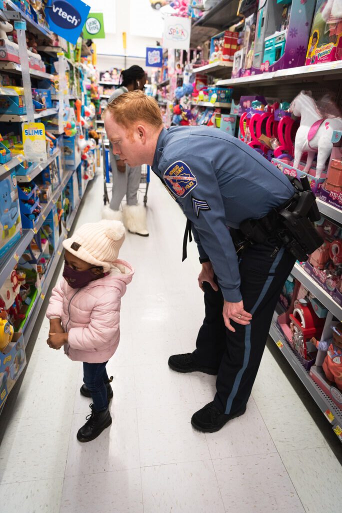 A police officer participating in Shop With A Cop program offers reassurance to a little girl within a toy store.