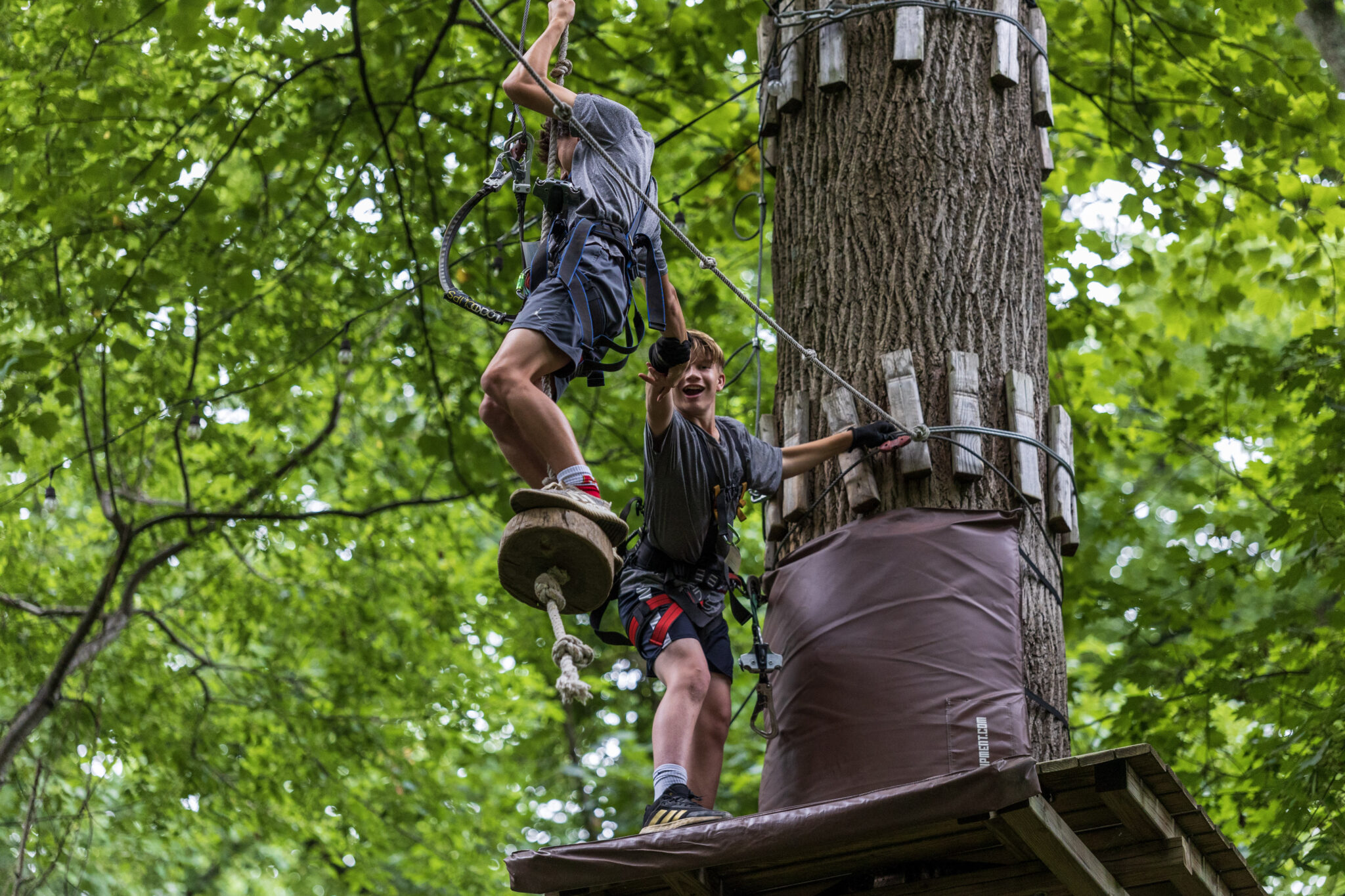Two boys participating in the P.L.E.D.G.E. Leadership Program on a ropes course in the woods.