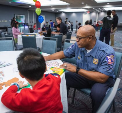 A firefighter sits at a table with a child at the HoCo Kids Holiday Party.