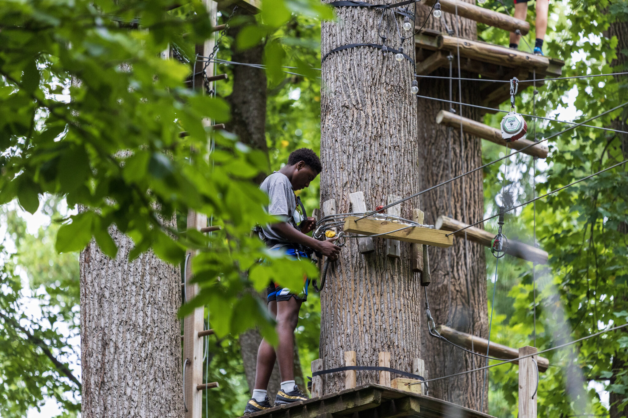 A man participating in the P.L.E.D.G.E. Leadership Program navigating a challenging ropes course set in the picturesque woods.