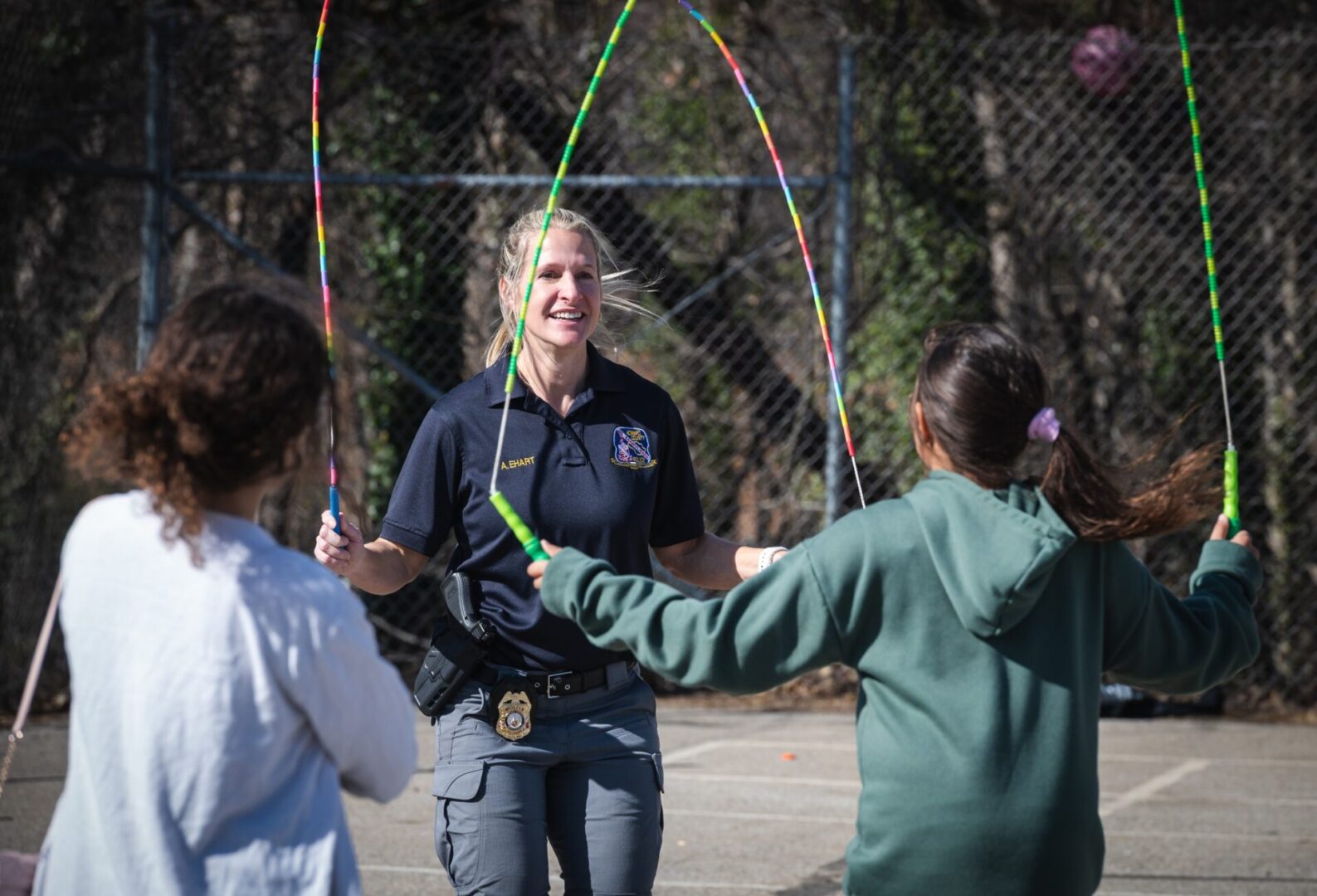 A police officer engages in a community athletic program with a group of girls, participating in a lively hula hoop session.
