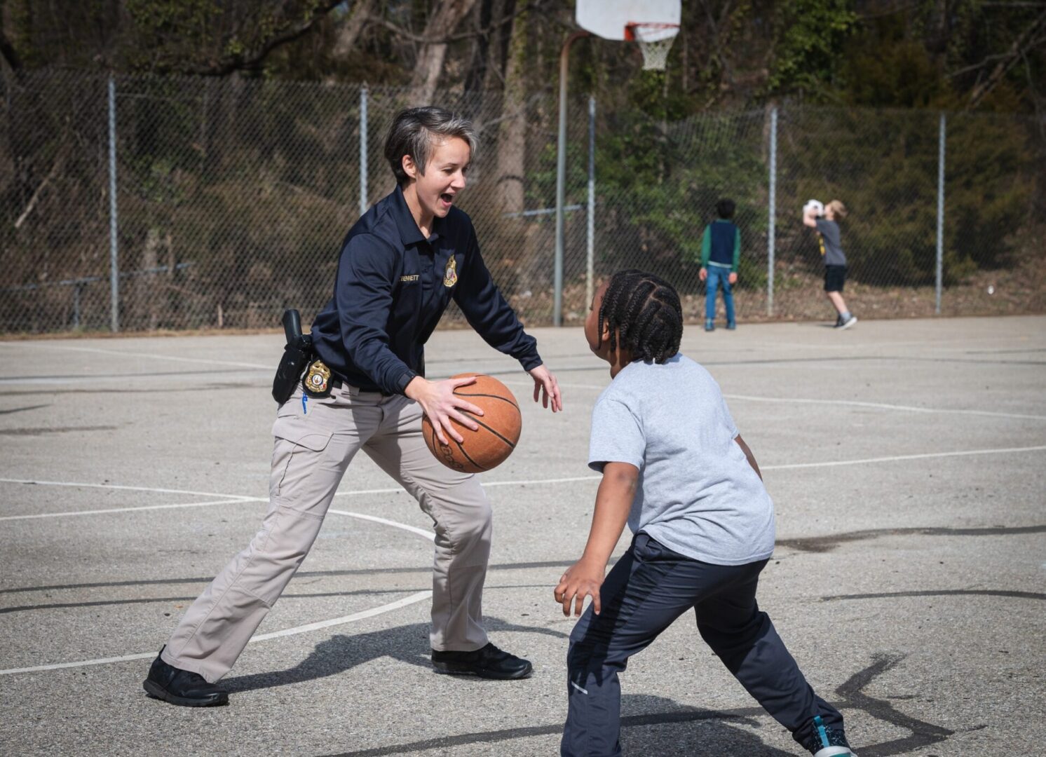 A police officer is participating in a community athletic program, playing basketball with a young boy.