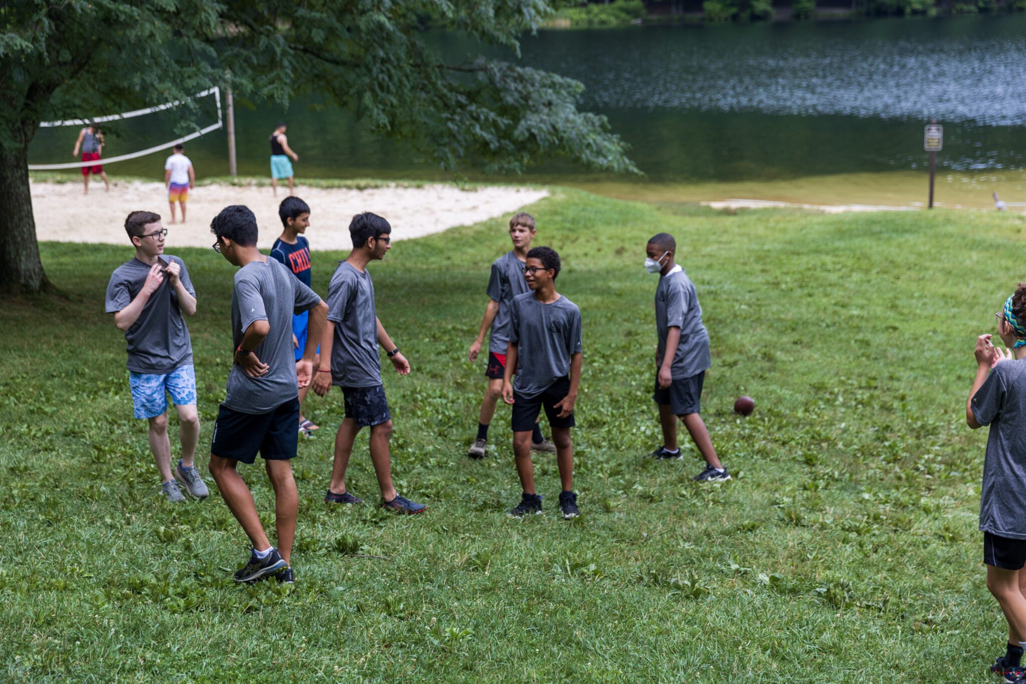 A group of boys participating in the P.L.E.D.G.E. Leadership Program playing a game of frisbee on a grassy field.