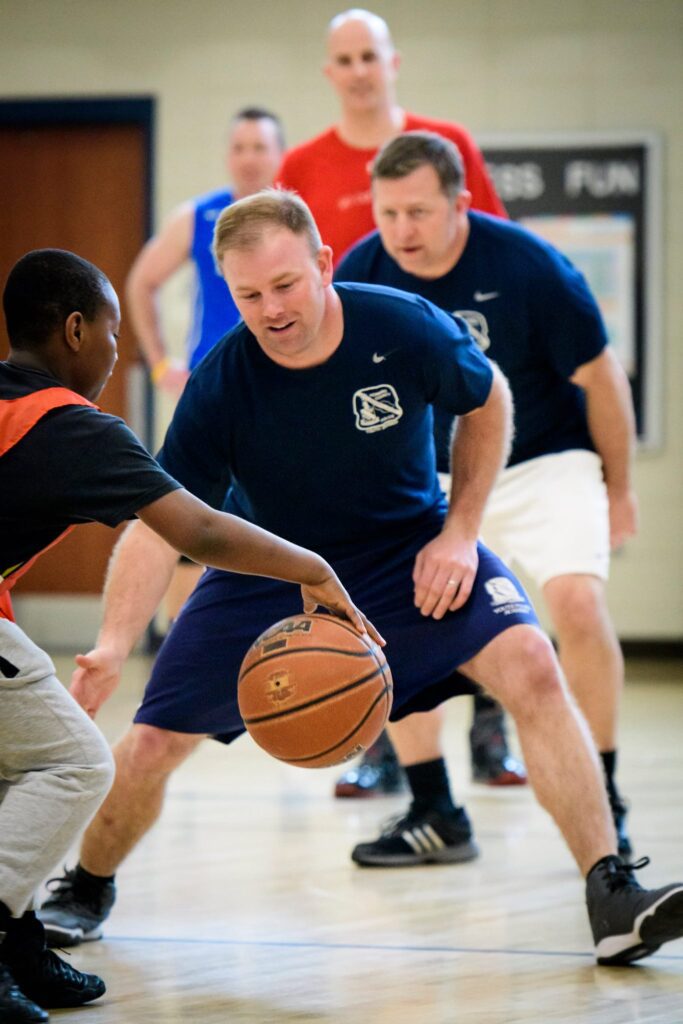 A man in a blue shirt is engaging in a community athletic program by playing basketball with a young boy.
