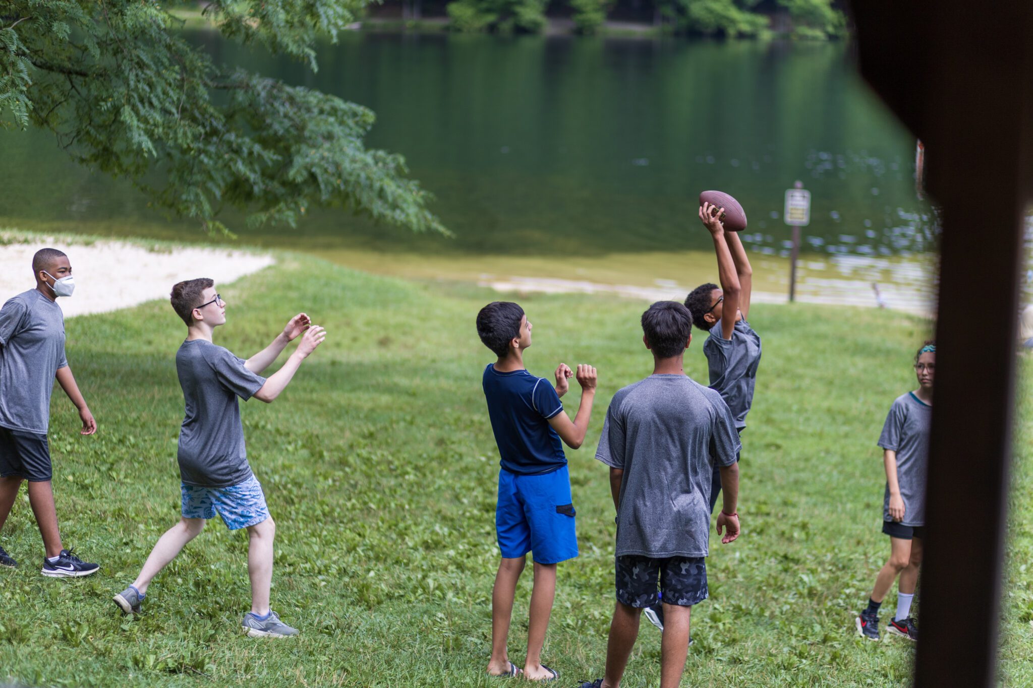 A group of boys participating in the P.L.E.D.G.E. Leadership Program, playing football in a grassy area near a lake.