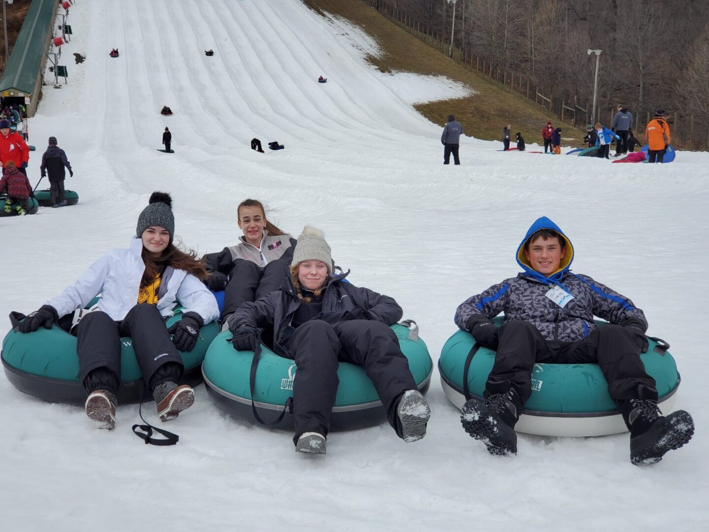 A P.L.E.D.G.E. Leadership Program group enthusiastically riding down a snow slope on tubes.