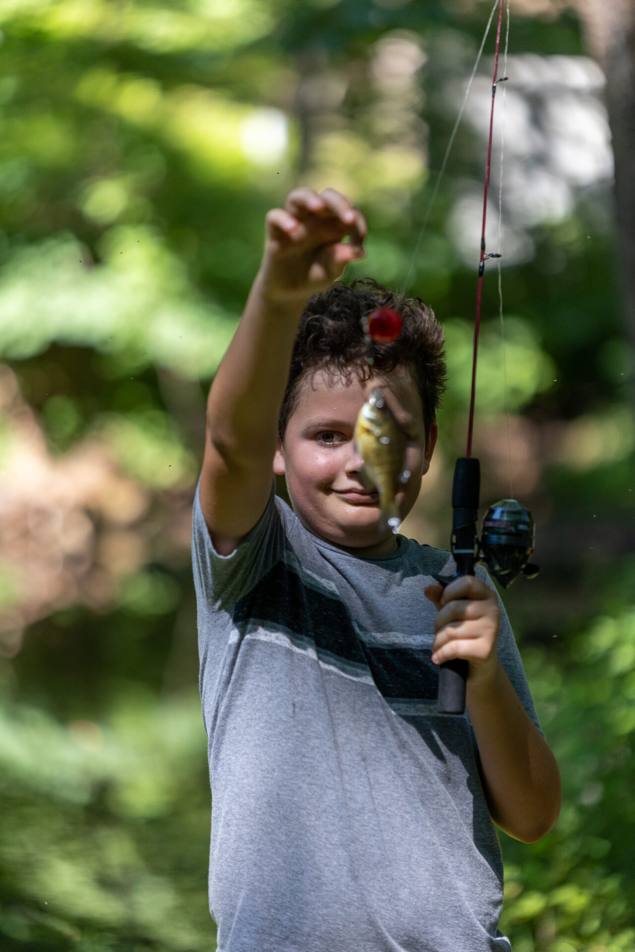 A young boy holding a fishing rod and proudly displaying a fish he caught.
