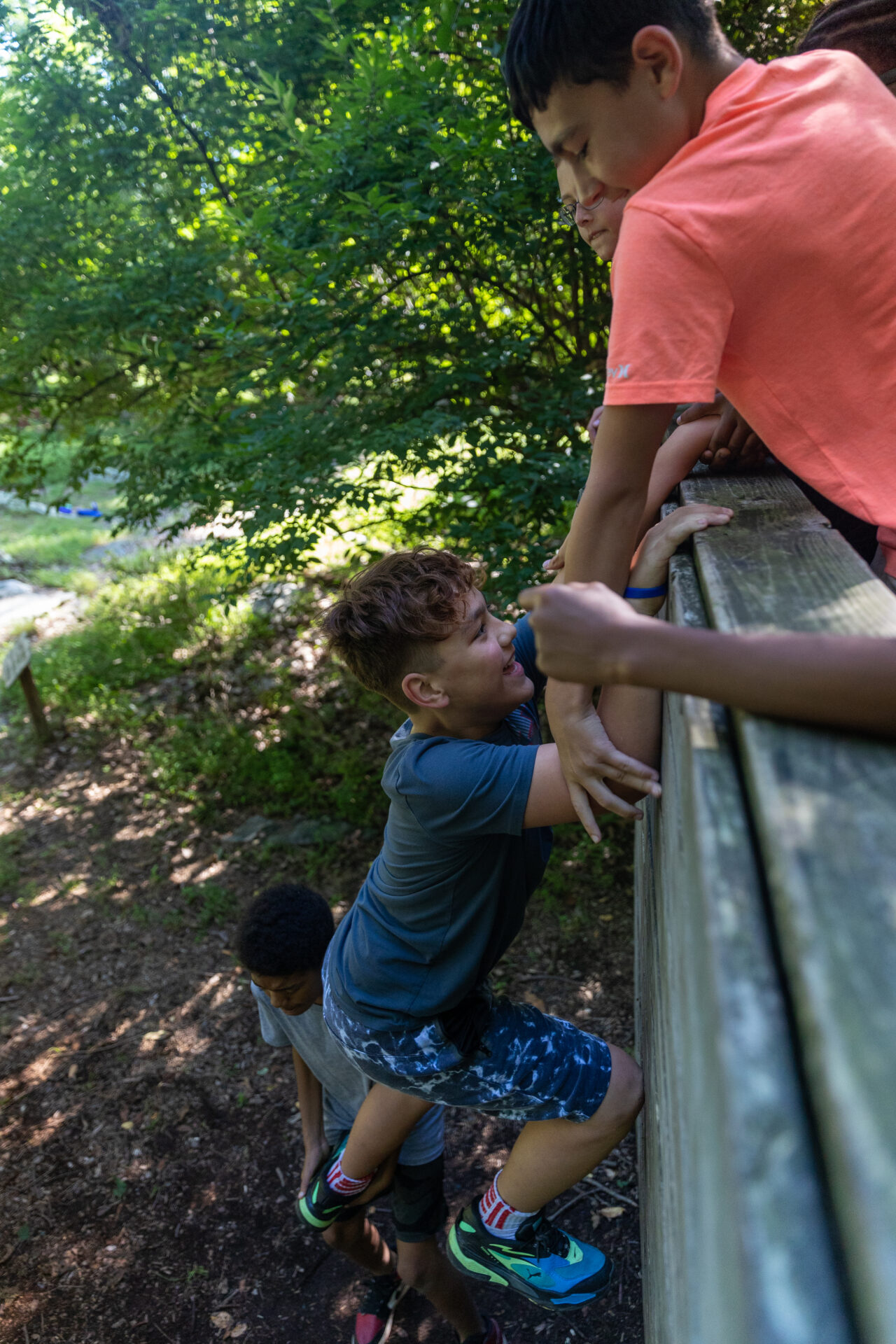 A group of kids having fun while climbing on a wooden railing in a wooded area known as BearTrax.