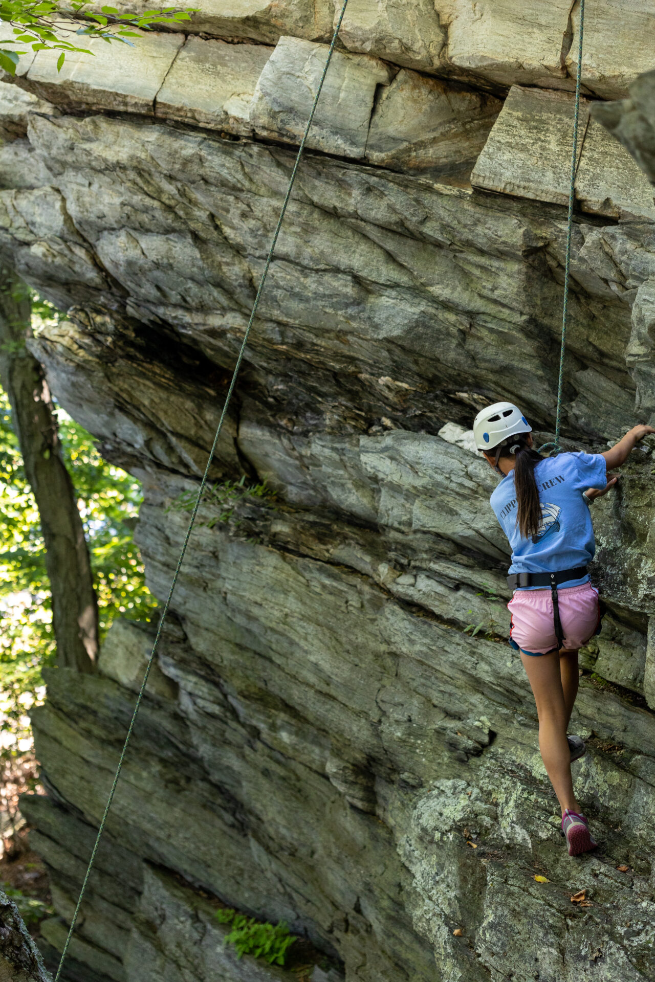 Using her BearTrax gear, a woman fearlessly climbs up a treacherous cliff.