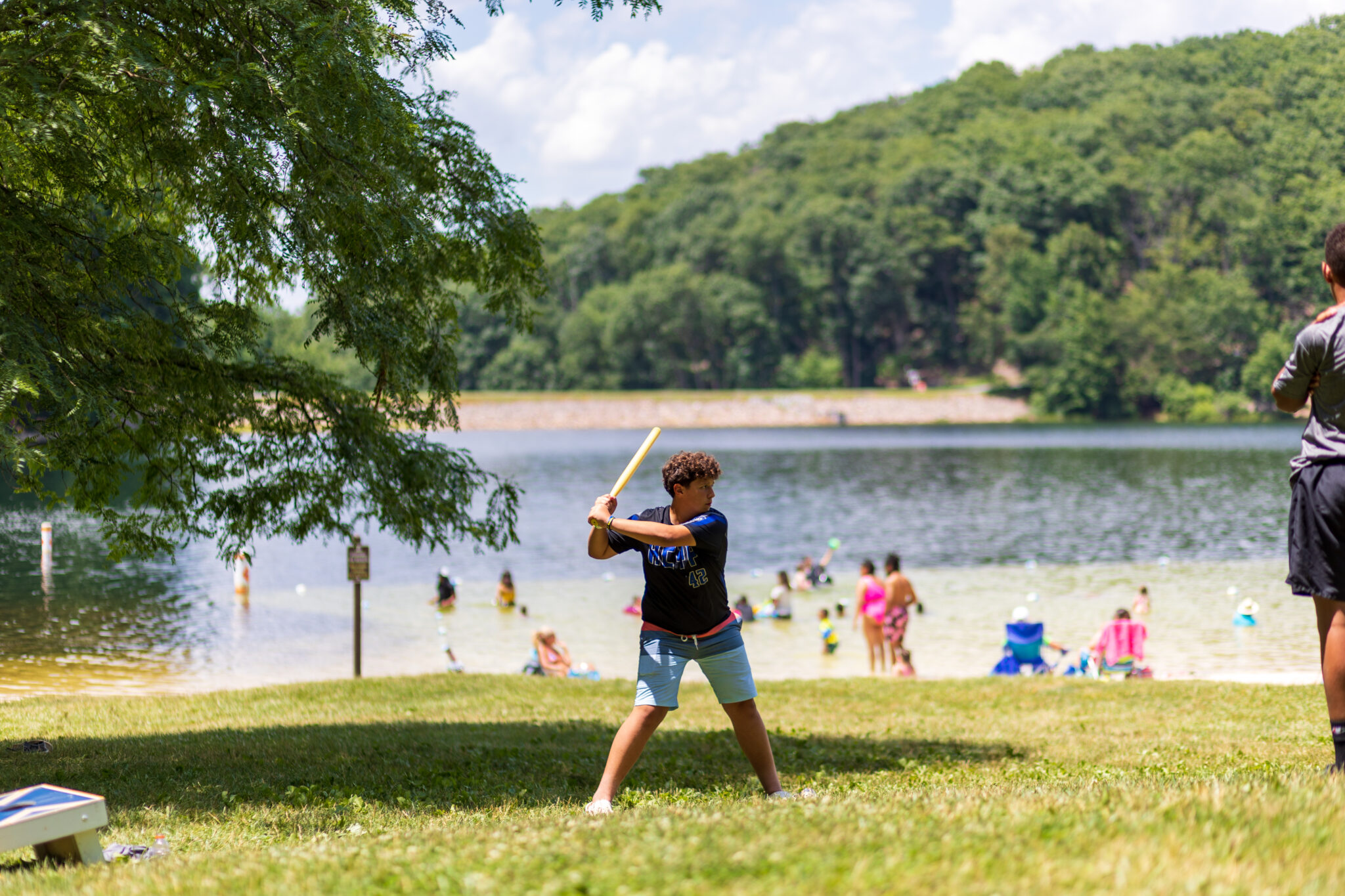 A boy participating in the P.L.E.D.G.E. Leadership Program is swinging a bat in front of a lake.