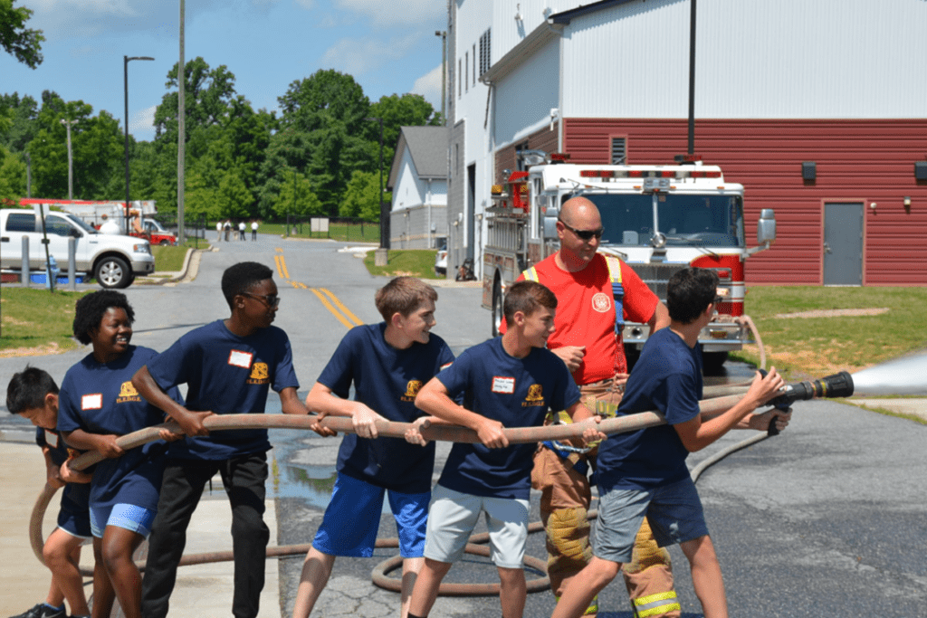 A group of boys participating in the P.L.E.D.G.E. Leadership Program, playing with a fire hose.