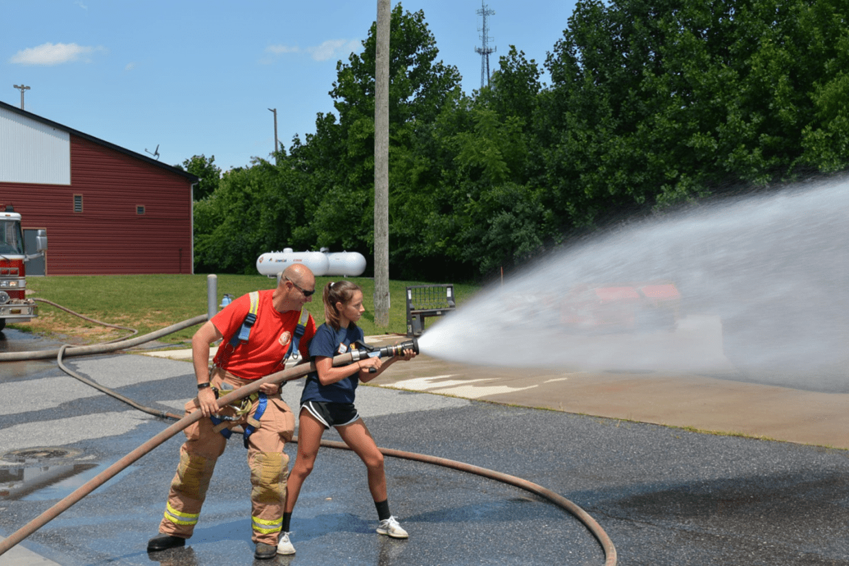 Two participants of the P.L.E.D.G.E. Leadership Program spraying water with a hose.