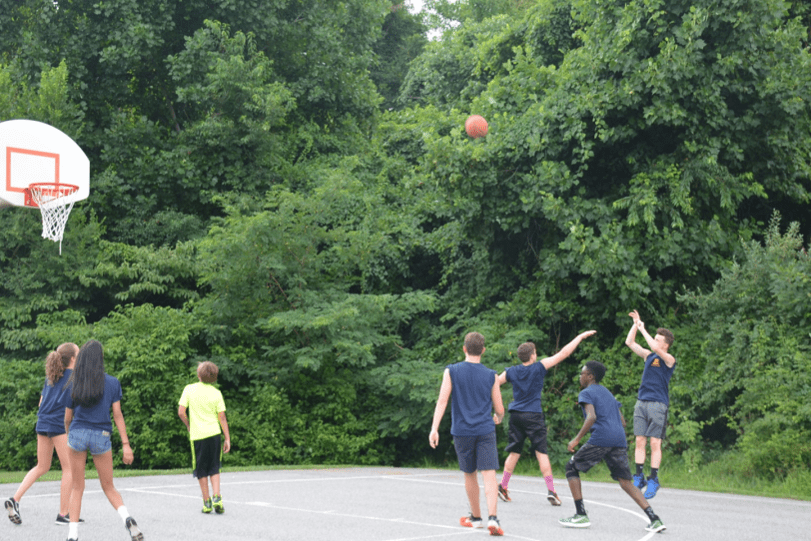 A group of kids participating in the P.L.E.D.G.E. Leadership Program while playing basketball on a basketball court.