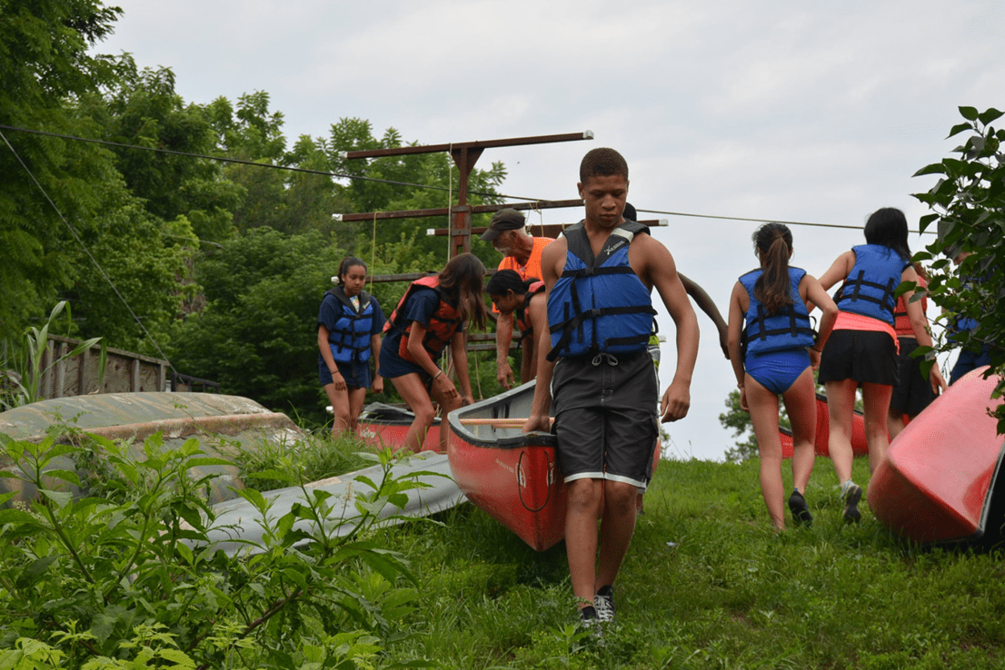 A group of people participating in the P.L.E.D.G.E. Leadership Program while carrying canoes.