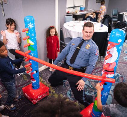 A group of children playing a game at the HoCo Kids Holiday Party with a police officer.