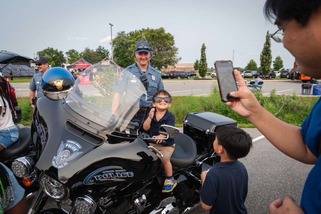 A man captures a moment of joy as he photographs a child on a motorcycle during National Night Out.