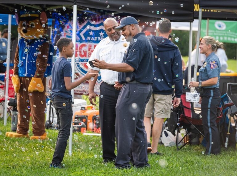 A group of people participating in National Night Out celebrations, standing in a grassy area while enjoying soap bubbles.