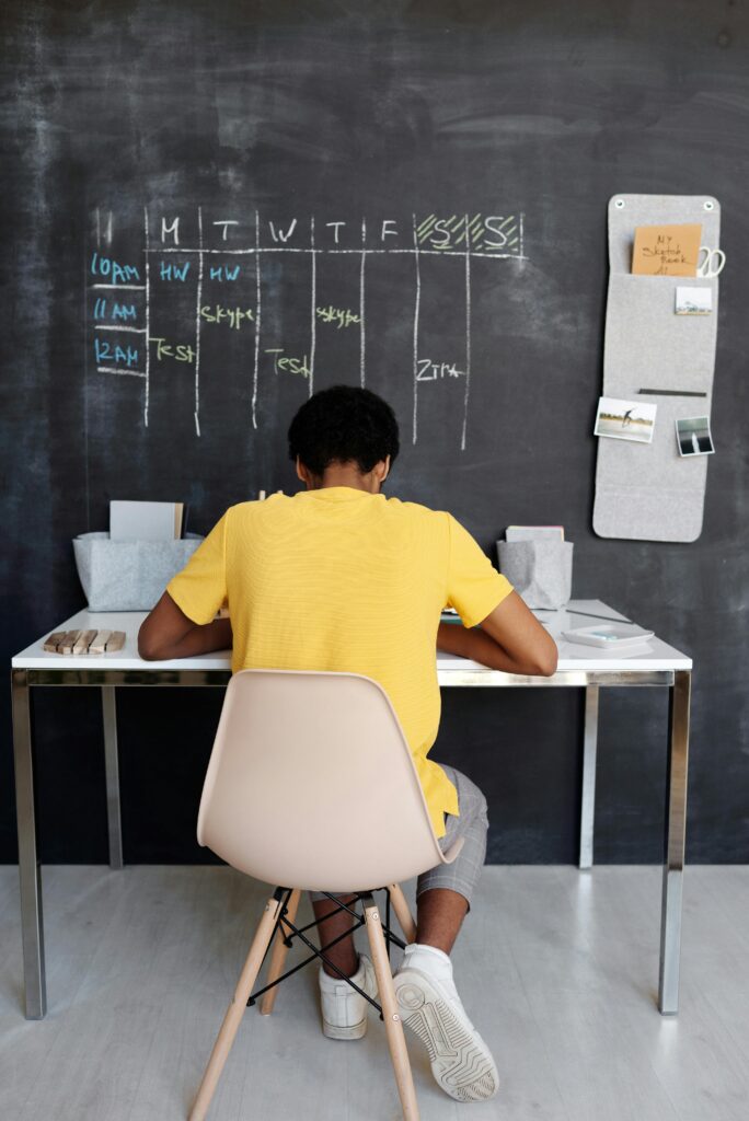 A boy sitting at a desk writing on the chalkboard.