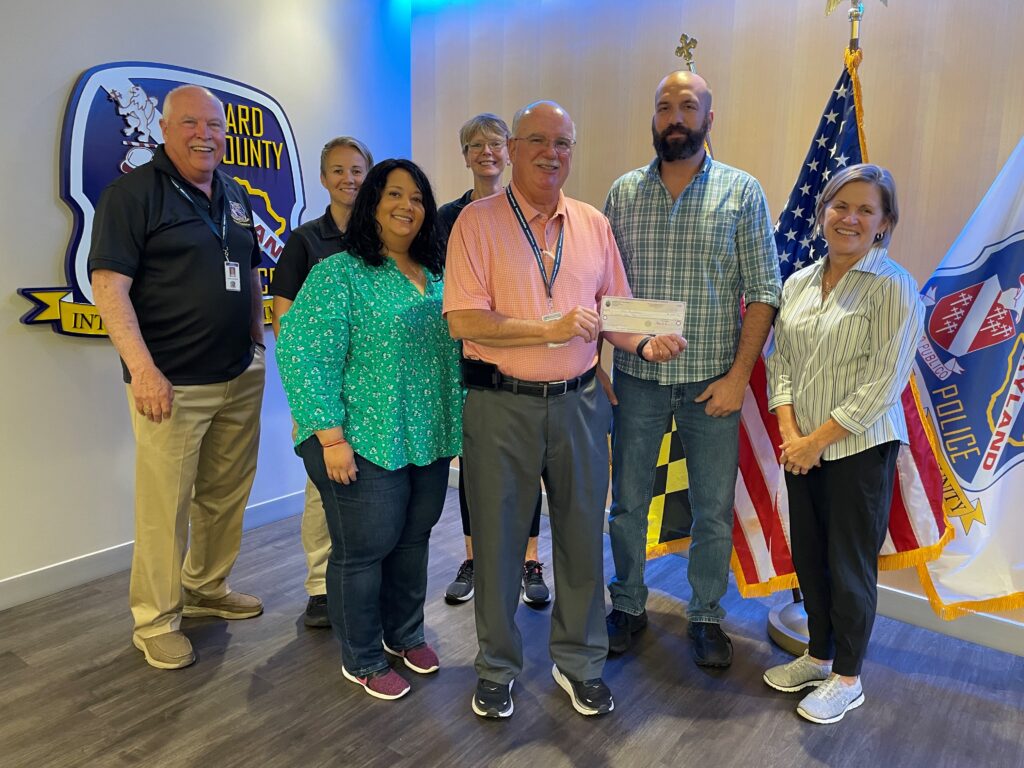 Group of six people posing with a check in front of American flags.