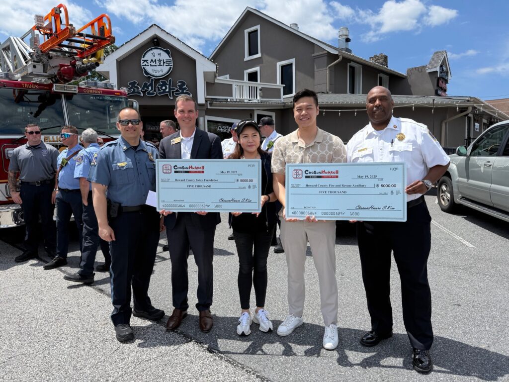 Group holding large checks outdoors in front of houses.