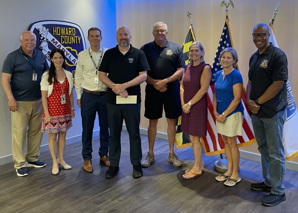 Group photo of six adults standing indoors, some in casual attire.