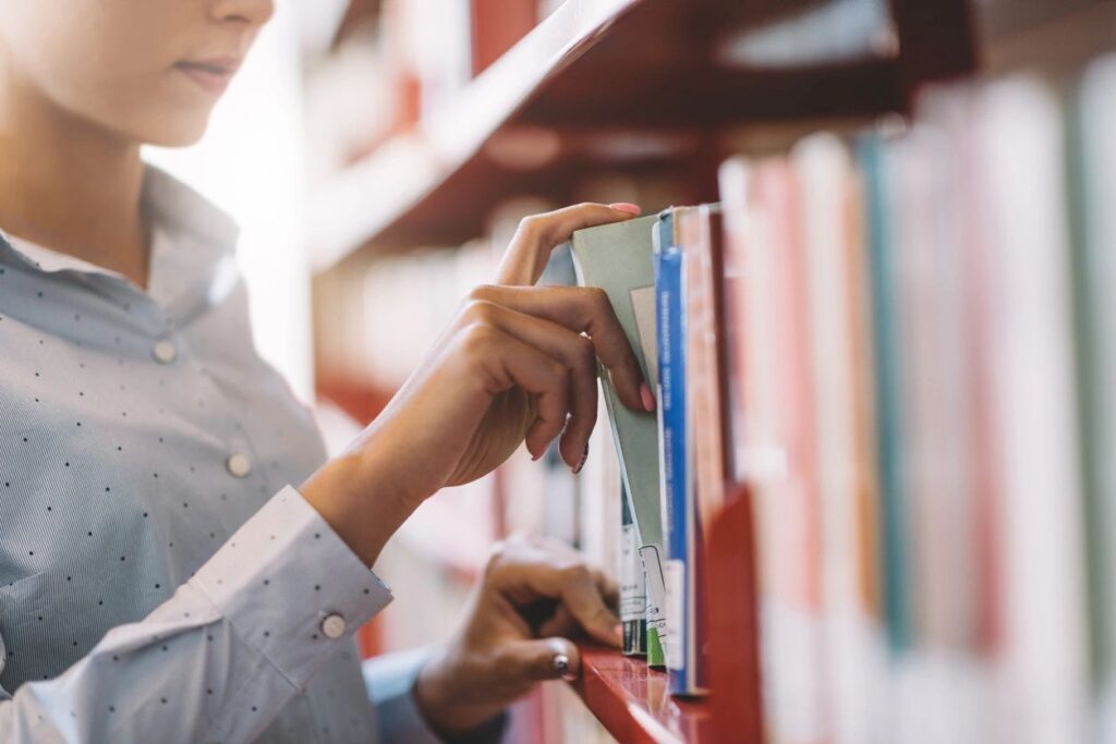 Person picking a book from a library shelf.